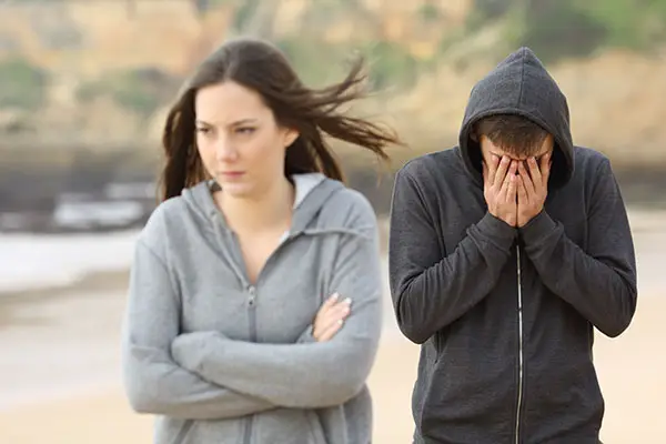 A young couple are breaking up, the girl walks away, the boy has his face in his hands