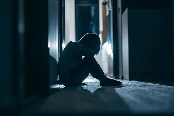 Side view of a crying little boy sitting in a dark room at home. Back lit.