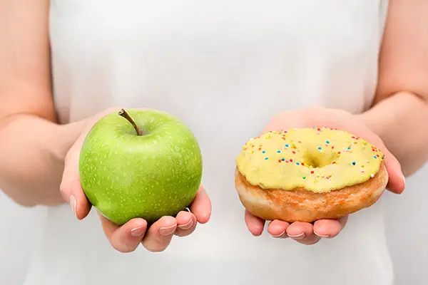 A woman holds an apple and a doughnut in either hand