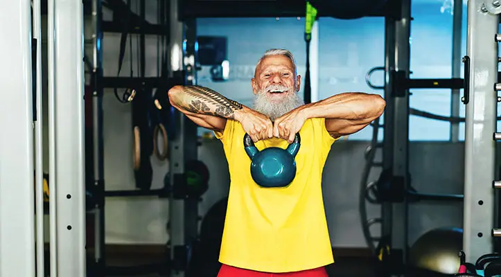 A happy bearded man in yellow lifts a weight in the gym
