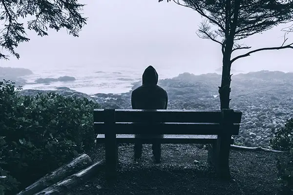 Sad and lonely hooded man sits overlooking the sea
