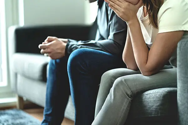 Man and woman sit on sofa, upset and troubled