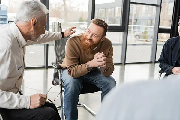 A mature man comforts a younger man at a group meeting
