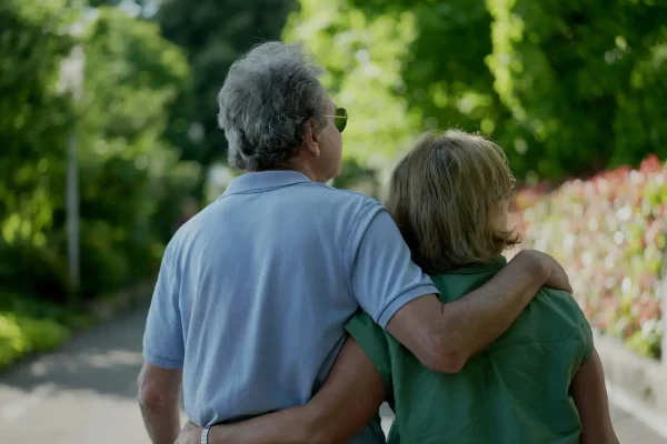 Romantic senior husband putting arm around wife, back view of older couple walking together in green path