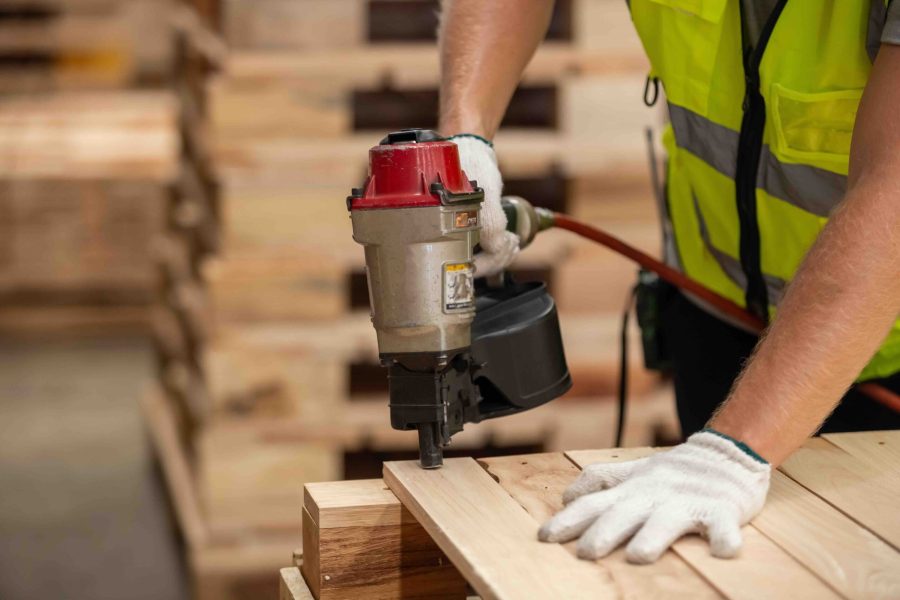 Engineer carpenter wearing safety uniform and yellow hard hat working using electric nail gun to on wood at workshop manufacturing.  Man worker wood warehouse industry.