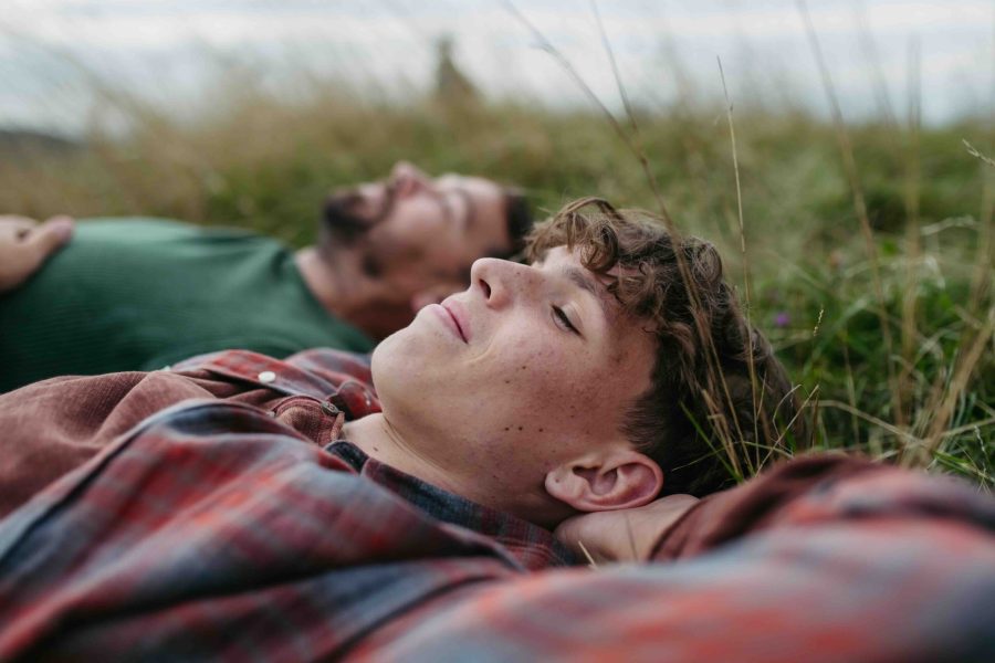 Top view of father and teen boy lying in grass and resting during hiking trip.