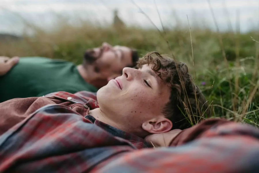Top view of father and teen boy lying in grass and resting during hiking trip.
